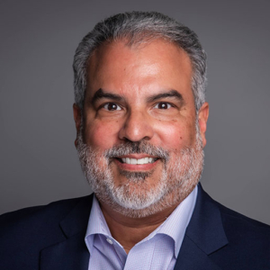 Headshot of Rigo J. Saborio in suit jacket and button up shirt, hands folded in front of him